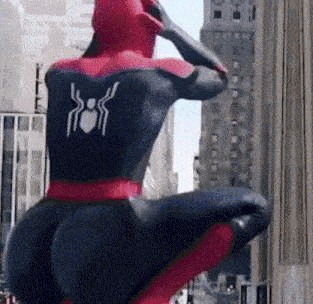 a man in a spiderman costume is kneeling down in front of a building in the city .