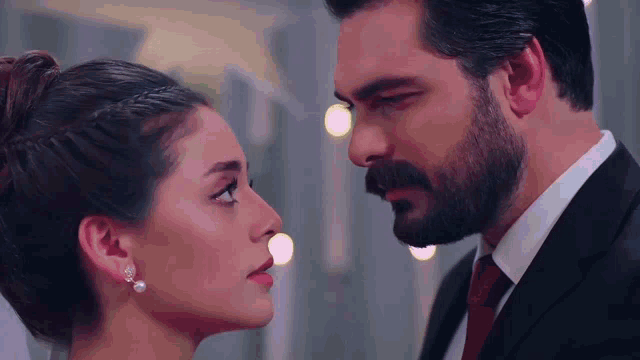 a man with a beard and a woman with pearl earrings look at each other