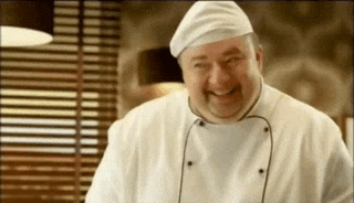 a man in a chef 's uniform and hat is smiling in a kitchen .