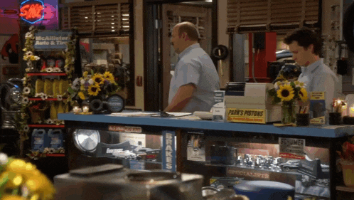 two men standing at a counter in a store with a sign that says sale on it