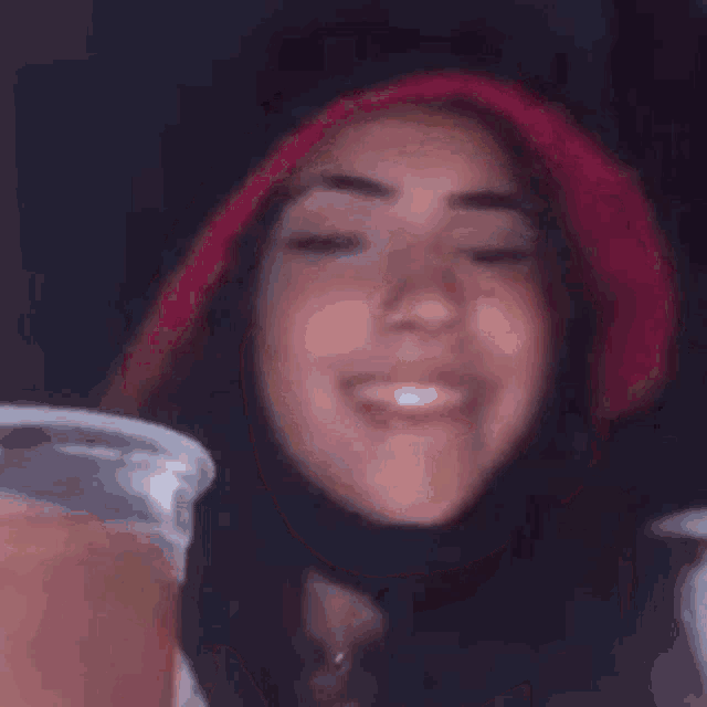a woman wearing a red hat and a mask is holding a cup of beer .