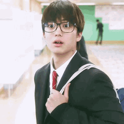 a young man wearing glasses and a suit and tie is holding a backpack .