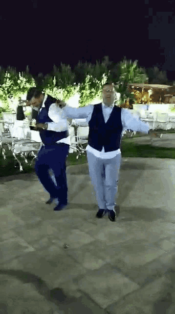two men in suits are dancing on a tiled floor at night