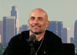 a bald man is sitting in front of a shure microphone in front of a city skyline