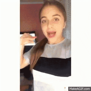 a girl is making a funny face while standing in front of a computer screen .