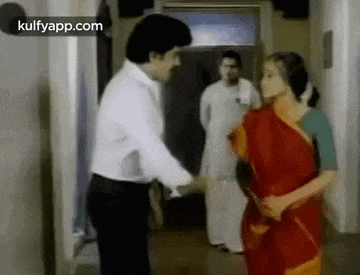 a man and a woman are shaking hands in a hallway . the woman is wearing a red saree .