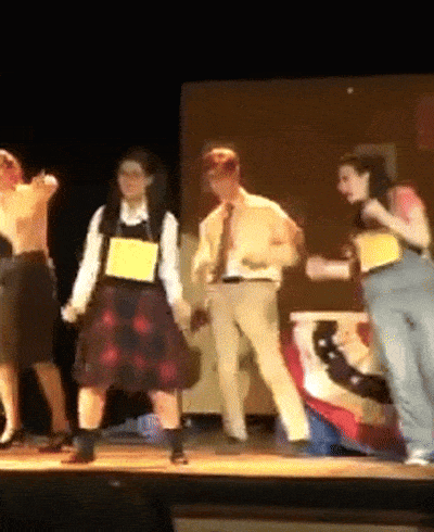 a group of people are dancing on a stage and one has a yellow tag on her chest