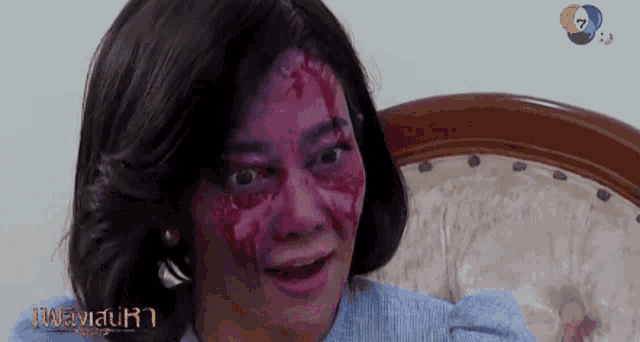 a woman with blood on her face is sitting in a chair with a tv channel behind her
