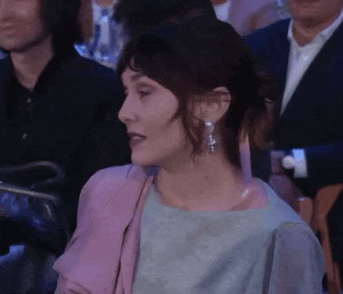 a woman wearing a purple jacket and earrings sits in a crowd of people