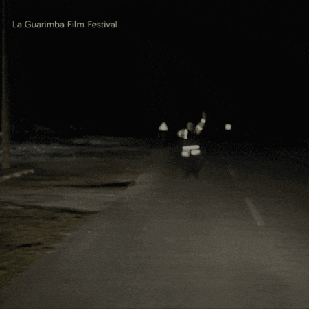 a poster for the la guarimba film festival shows a man walking down a road at night