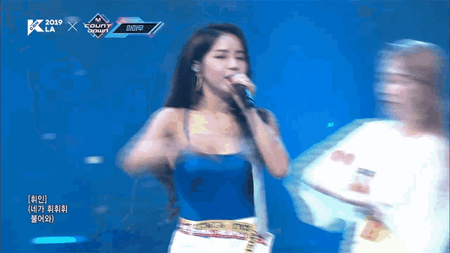 a woman singing into a microphone on a stage in front of a sign that says 2019
