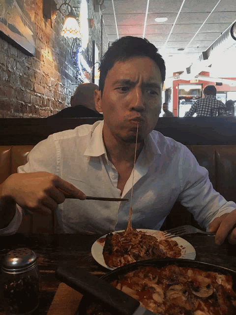 a man in a white shirt is eating spaghetti with a fork and making a funny face