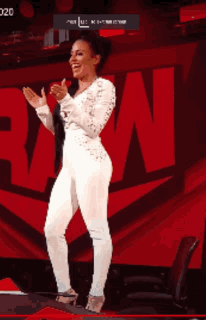 a woman in a white jumpsuit is clapping her hands in front of a large red n.