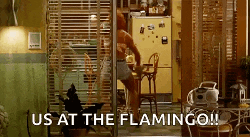 a woman is standing on a table in a kitchen with the words `` us at the flamingo '' written on the screen .