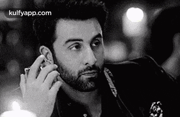 a black and white photo of a man with a beard talking on a cell phone .