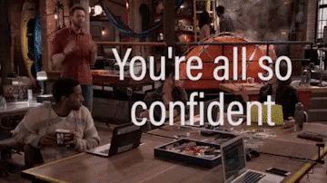 a group of people are sitting at a table with laptops and a sign that says you 're all so confident