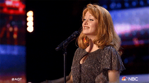a woman singing into a microphone with the nbc logo on the bottom