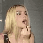 a woman is applying lipstick to her lips while looking at herself in the mirror .
