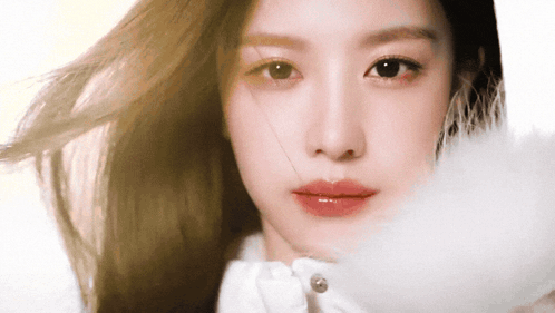 a close up of a woman 's face with a white feather in her hand