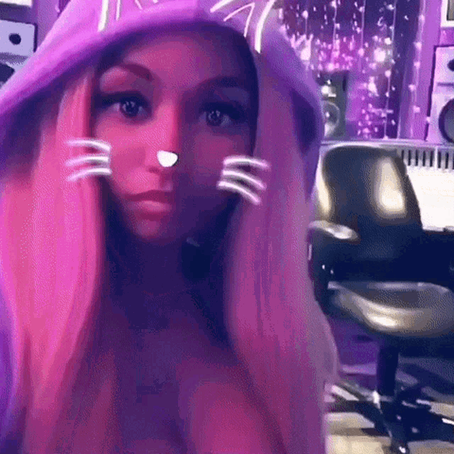 a woman with pink hair is wearing a purple cat hoodie and looking at the camera .