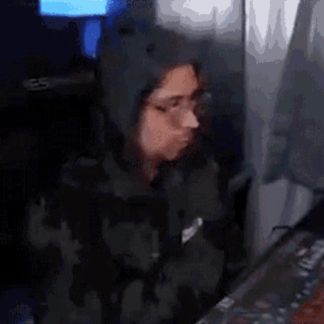 a woman wearing a hoodie and glasses is sitting in front of a keyboard .
