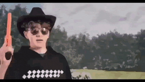 a man wearing a cowboy hat and sunglasses is holding a toy gun .