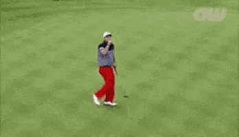 a man in a striped shirt and red pants is holding a golf club on a green field .