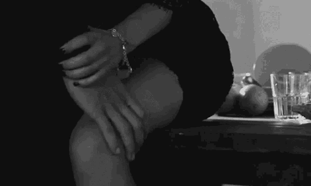 a woman in a black dress is sitting at a table with her legs crossed and her hands on her knees .