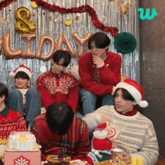 a group of people wearing santa hats and sweaters are sitting in front of a sign that says holiday