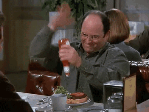 a man is sitting at a table holding a bottle of ketchup and smiling .