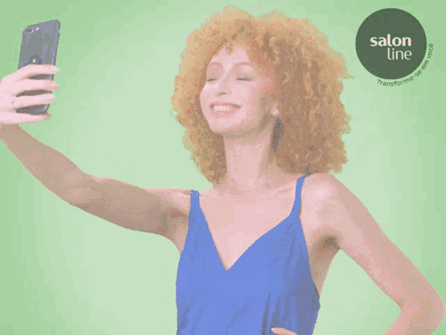 a woman in a blue dress taking a selfie with a salon line logo behind her