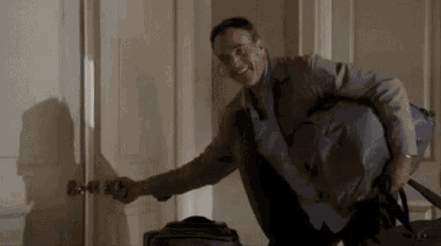 a man is holding a bag and opening a door in a room .