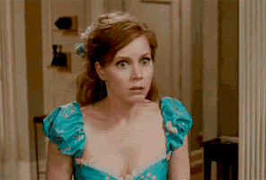 a woman in a blue dress with a flower in her hair is looking at the camera with a surprised look on her face .