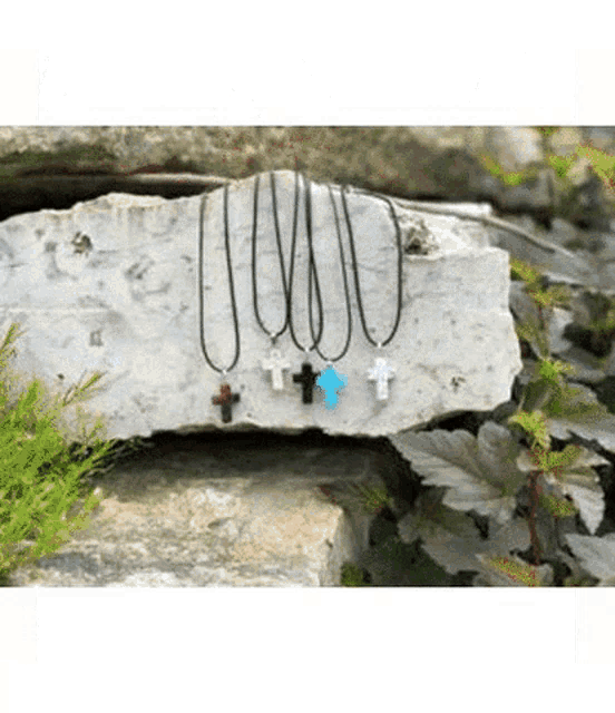 a group of cross necklaces sitting on top of a large rock .
