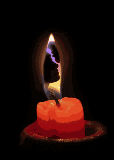 a burning candle with a silhouette of a woman in the background