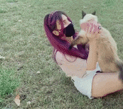 a woman with purple hair is holding a cat in her lap