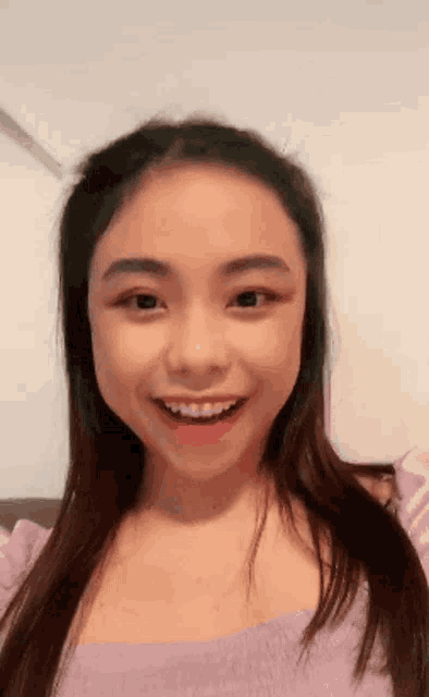 a young asian girl is smiling and wearing a purple top .