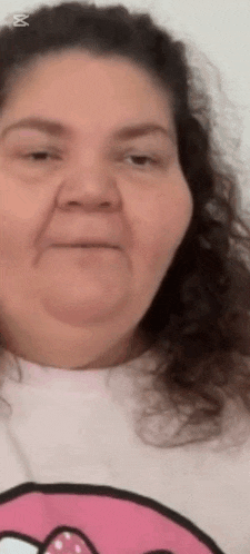 a woman with curly hair is wearing a pink sweater with a donut on it and making a funny face .
