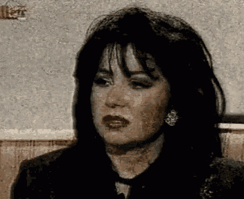 a woman with long black hair is sitting on a couch and making a funny face .