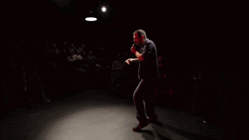 a man in a black shirt stands on a stage with a microphone