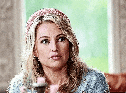 a woman wearing a headband and a blue sweater is sitting in front of a window .