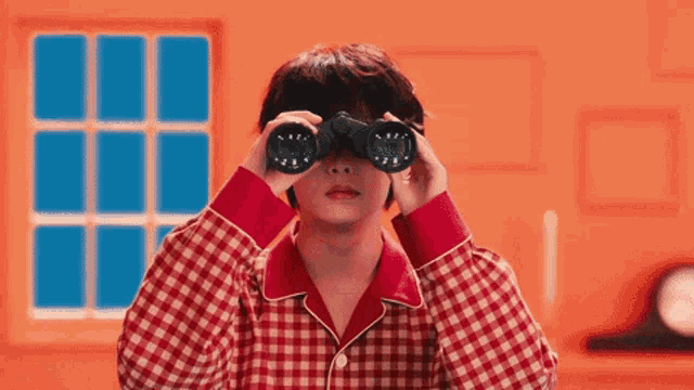 a young man in pajamas is looking through binoculars in front of a window .