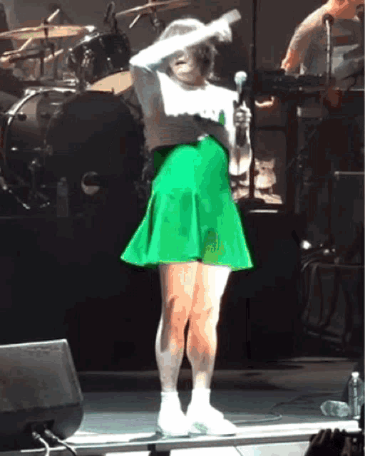 a woman in a green skirt is singing into a microphone on a stage