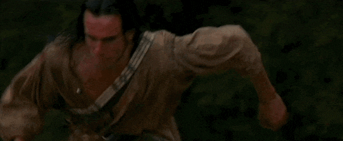 a man with long hair is walking in the dark with a guitar strap around his neck .