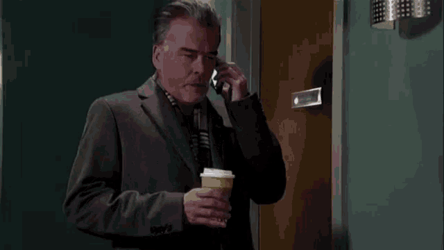 a man in a suit is holding a cup of coffee and talking on a cell phone