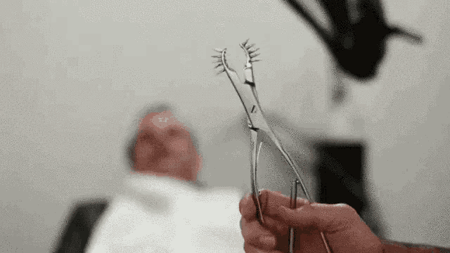 a person is holding a pair of scissors in front of a man laying on a bed .