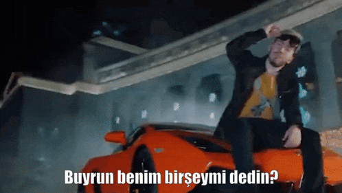 a man sitting on top of an orange sports car with the words buyrun benim birseymi dedin written below him