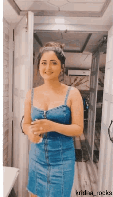 a woman in a denim dress is standing in front of a door with the name kridha_rocks on the bottom