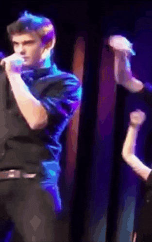 a man in a black shirt is singing into a microphone on a stage