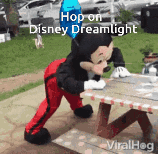 a mickey mouse mascot is standing on a picnic table with a blue balloon